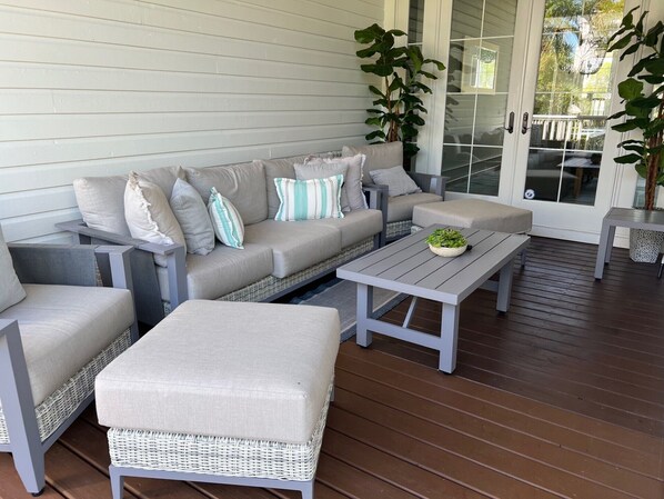 A covered porch with a grey sofa set, two armchairs, a coffee table, and potted plants. - Luxury coastal home pool/spa, 1 block downtown AMI Pine Ave & 0.2 mi to beach (Anna Maria)