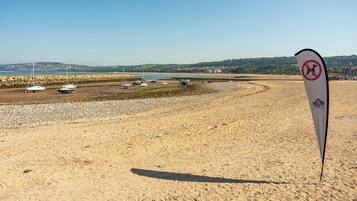 A sandy beach with boats and a no swimming sign.