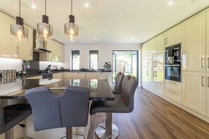 Une cuisine moderne dotée d’un îlot central, de luminaires suspendus et offrant une vue sur l’extérieur.