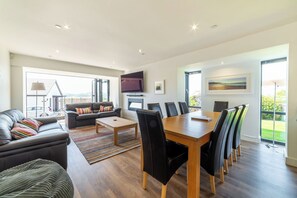 Un salon moderne avec un canapé, une table basse et une table à manger avec des chaises. Un téléviseur est fixé au mur et une fenêtre offre une vue dégagée.