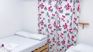 Una habitación con dos camas, una sobre un palé de madera y la otra sobre una estructura metálica. Hay un equipo de aire acondicionado blanco en la pared.