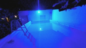 Una piscina con una escalera y una estructura iluminada en azul al fondo.