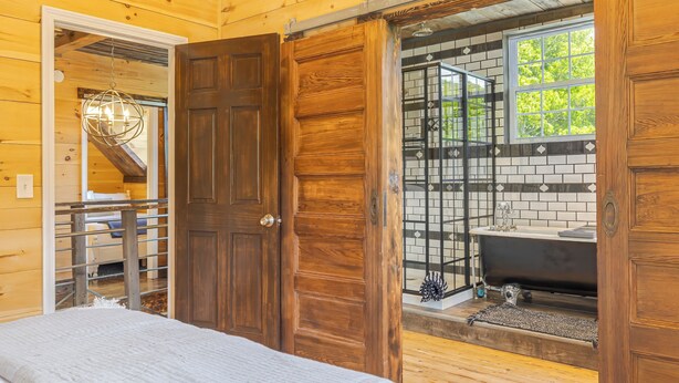 A wooden interior with a bed, a sliding door to a bathroom with a bathtub, and a staircase leading to another room. - Old Maine style w/ modern amenities - dog friendly (Sullivan)
