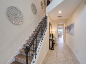 Staircase leads to an upper level, surrounded by decorative wall art and light-colored tiles.