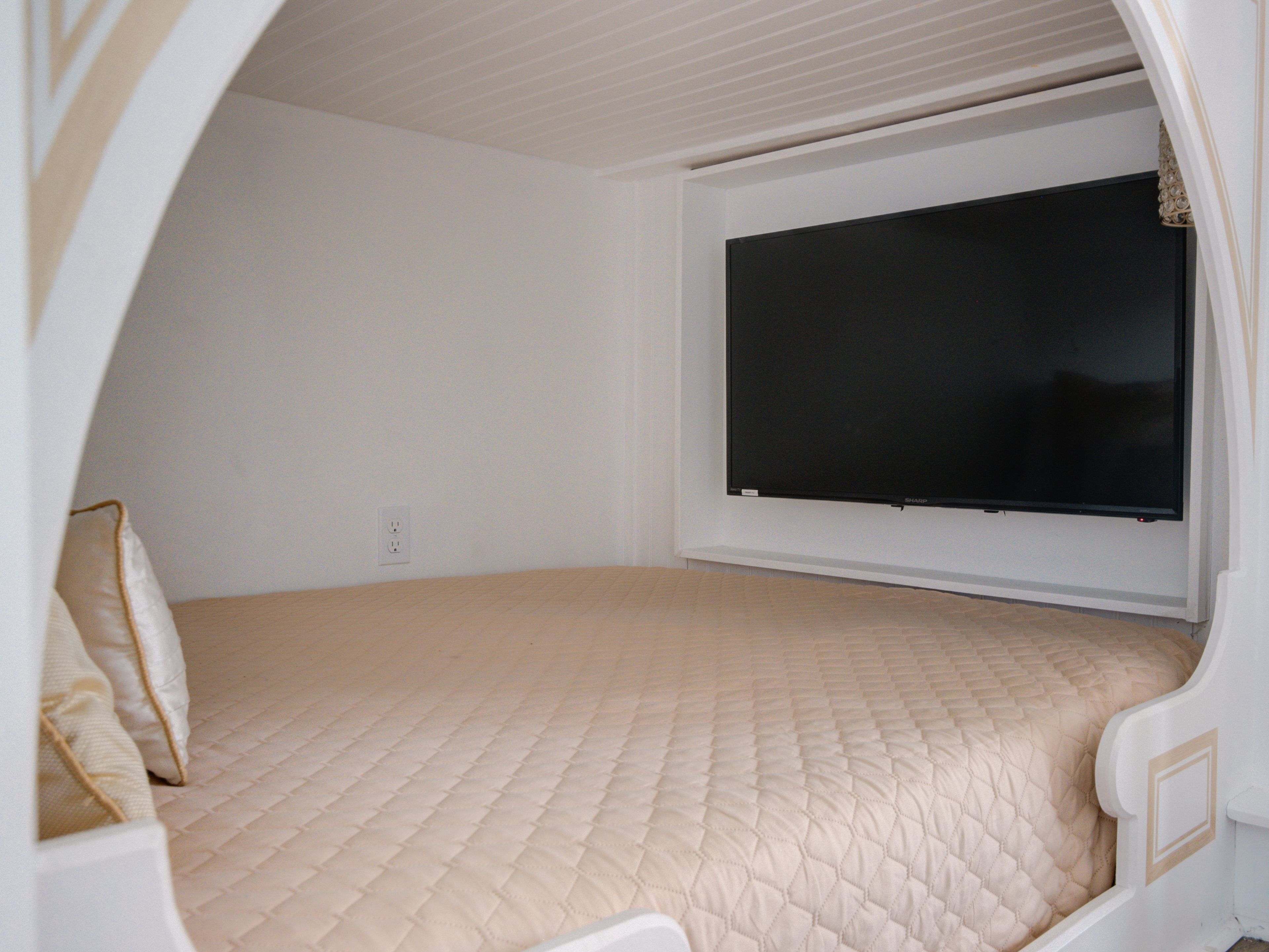 A bedroom with a bed, a television mounted on the wall, and a window.