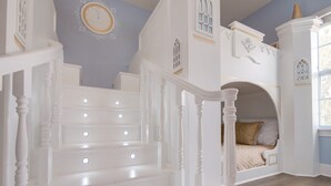 Un escalier avec des balustrades blanches et des luminaires, menant à une chambre à coucher équipée d’un lit et d’une fenêtre.