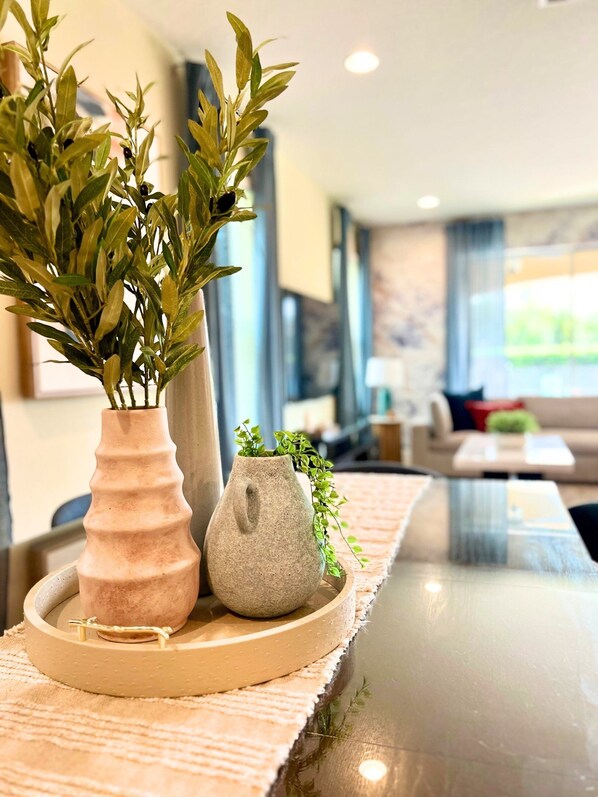A modern living room with a glass coffee table, a beige rug, and two vases with plants.