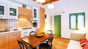 Een kleine keuken met houten kastjes, een eettafel met stoelen en een groene deur.