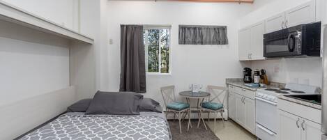A compact bedroom with a bed, a small dining table, and a kitchenette.