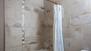 Un baño con bañera, ducha y pared de azulejos.