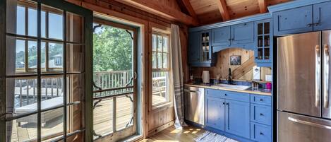 Cocina de cabaña de madera con ventanas amplias, un refrigerador de acero inoxidable y armarios azules.