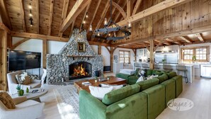 A spacious living room with a stone fireplace, wooden beams, and a green sectional sofa.