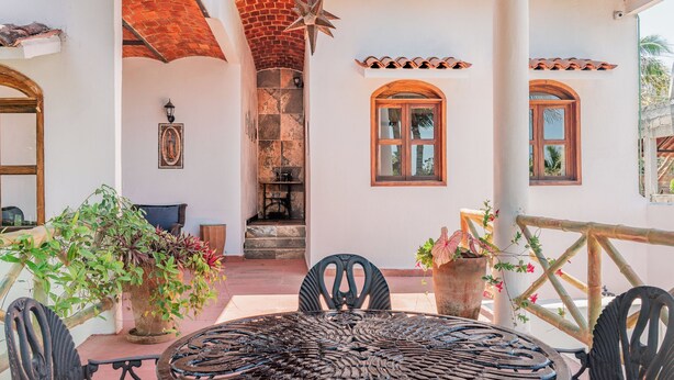 A patio with a round metal table and chairs, surrounded by potted plants and a brick wall.