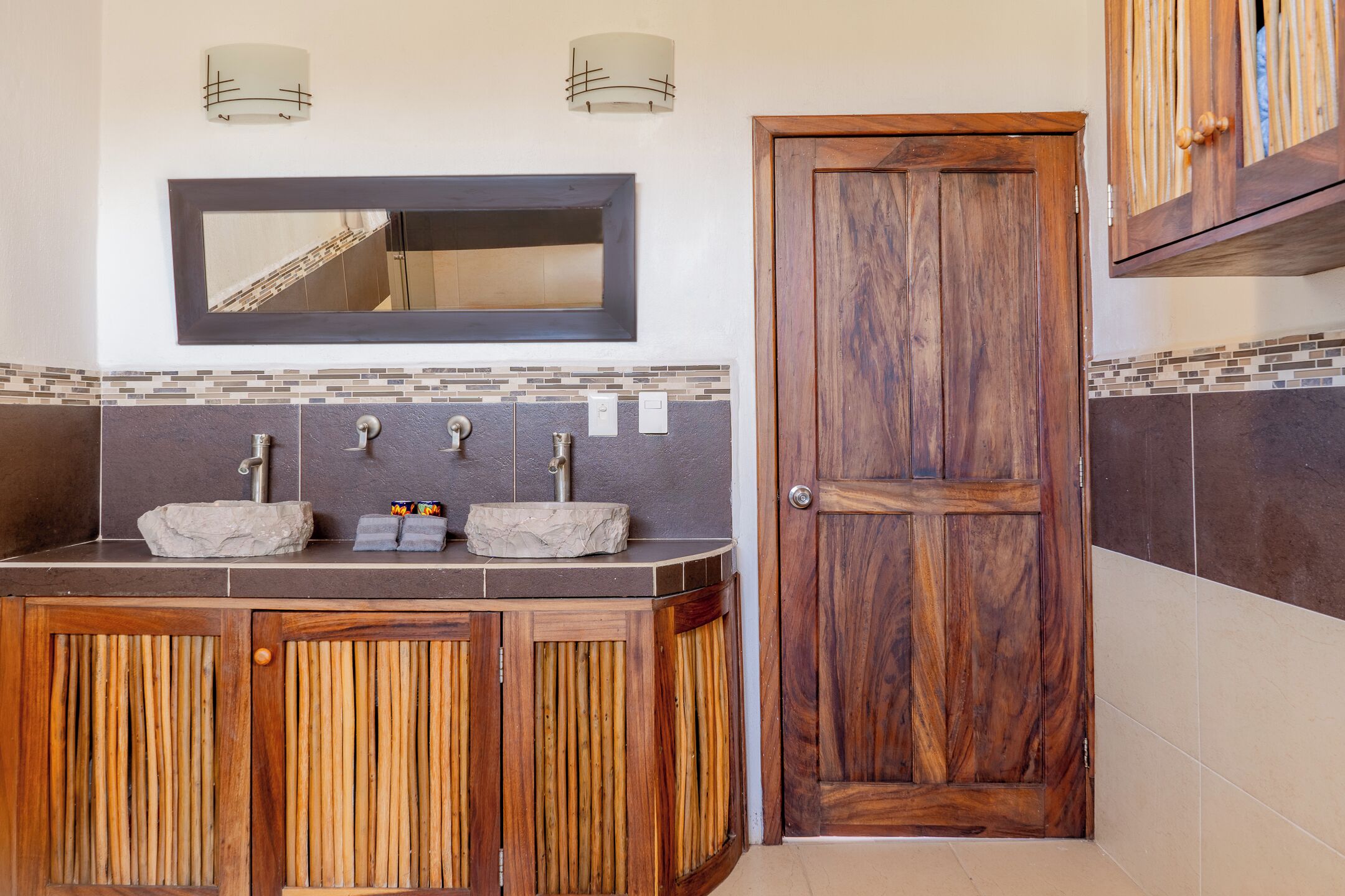 A bathroom with a wooden vanity, two sinks, a mirror, and a door.