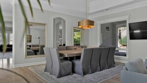 Een eetgedeelte met een ronde tafel, grijs gestoffeerde stoelen, een getextureerd vloerkleed en een hanglamp.