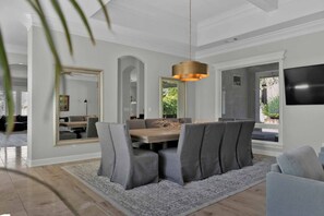 A dining area with a round table, grey upholstered chairs, a patterned rug, and a hanging pendant light.