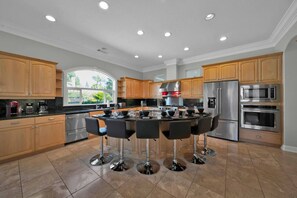 A modern kitchen with a central island, stainless steel appliances, wooden cabinets, and a large window.