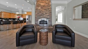 Een moderne woonkamer met een stenen openhaard, leren fauteuils en een keuken op de achtergrond.