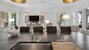 Un salon moderne doté d’un îlot central, de deux canapés en cuir, d’un téléviseur à écran plat et de luminaires suspendus.