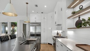 Une cuisine moderne dotée d’un îlot central, d’appareils électroménagers en acier inoxydable, de meubles blancs et d’un plancher en bois.