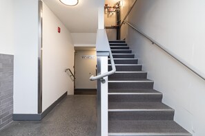 A staircase with a handrail, carpeted steps, and a wall-mounted sign indicating a garbage and recycling room.