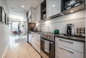 A modern kitchen with white cabinets, a stainless steel stove, and a coffee maker. - Spacious Patio and Funky Vibes in Old Town! (Victoria)