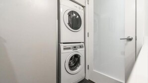 A laundry room with two stacked washing machines and a closed door. - Spacious Patio and Funky Vibes in Old Town! (Victoria)