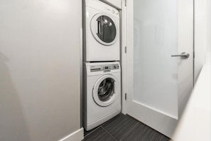 A laundry room with two stacked washing machines and a closed door. - Spacious Patio and Funky Vibes in Old Town! (Victoria)