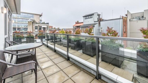 A balcony with a glass railing, a round table, and wicker chairs. - Spacious Patio and Funky Vibes in Old Town! (Victoria)