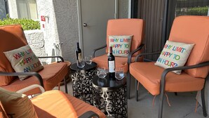 Un espace extérieur aménagé avec des chaises orange et une table ronde, chaque siège étant agrémenté d’un coussin sur lequel on peut lire : « POURQUOI LIMITER LE BONHEUR À UNE HEURE ? »
