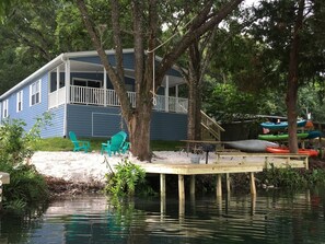Une maison avec une jetée qui s’avance sur un plan d’eau, entourée d’arbres.