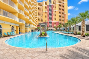 A hotel pool area with a circular pool, lounge chairs, and a large building in the background.