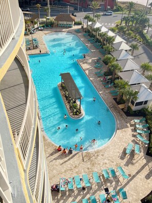 Una amplia piscina exterior con varias pistas, rodeada de tumbonas y palmeras.