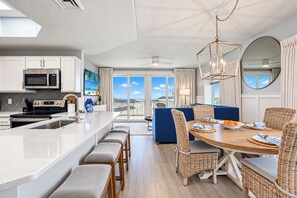 A modern kitchen with a central island, dining area with wicker chairs, and a view to the outside.