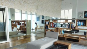 A modern library with a sofa, bookshelves, and a large window.