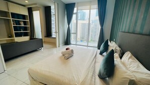A hotel room with a large bed, a built-in TV, a seating area with a sofa, and a view of tall buildings through the window.