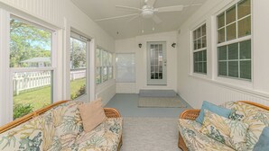 Eine überdachte Veranda mit zwei Korbsesseln, einem Deckenventilator und großen Fenstern.