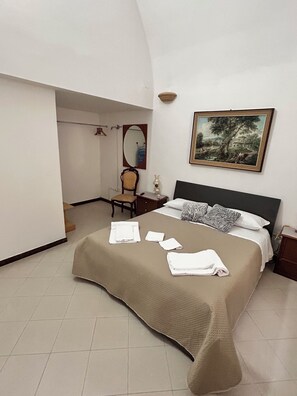 Un dormitorio con cama, escritorio, silla, espejo y un cuadro en la pared.