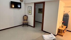 A hotel room with a flat-screen TV mounted on the wall, a wooden chair, a framed picture, a doorway leading to another room, and towels on the bed. - Accogliente Casa per Famiglie, Gruppi e Animali Domestici (Matera)