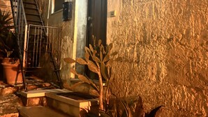 A building with a textured exterior, a door, and a staircase leading to an upper level. There are potted plants in front of the building. - Accogliente Casa per Famiglie, Gruppi e Animali Domestici (Matera)