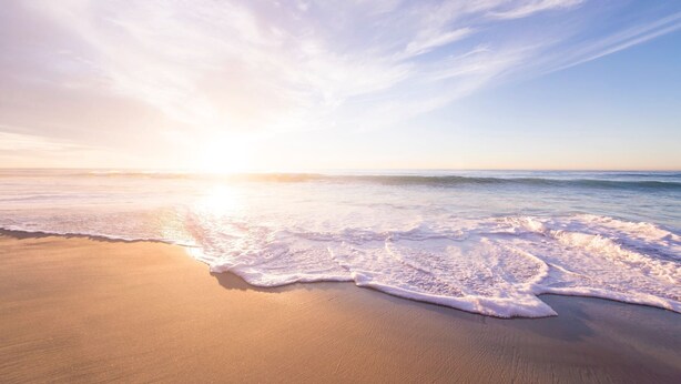 A beach with waves gently lapping onto the shore under a clear sky.