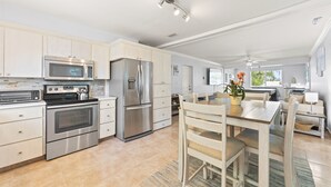 A modern kitchen with stainless steel appliances, a dining area with a wooden table and chairs, and a view of the outdoors.