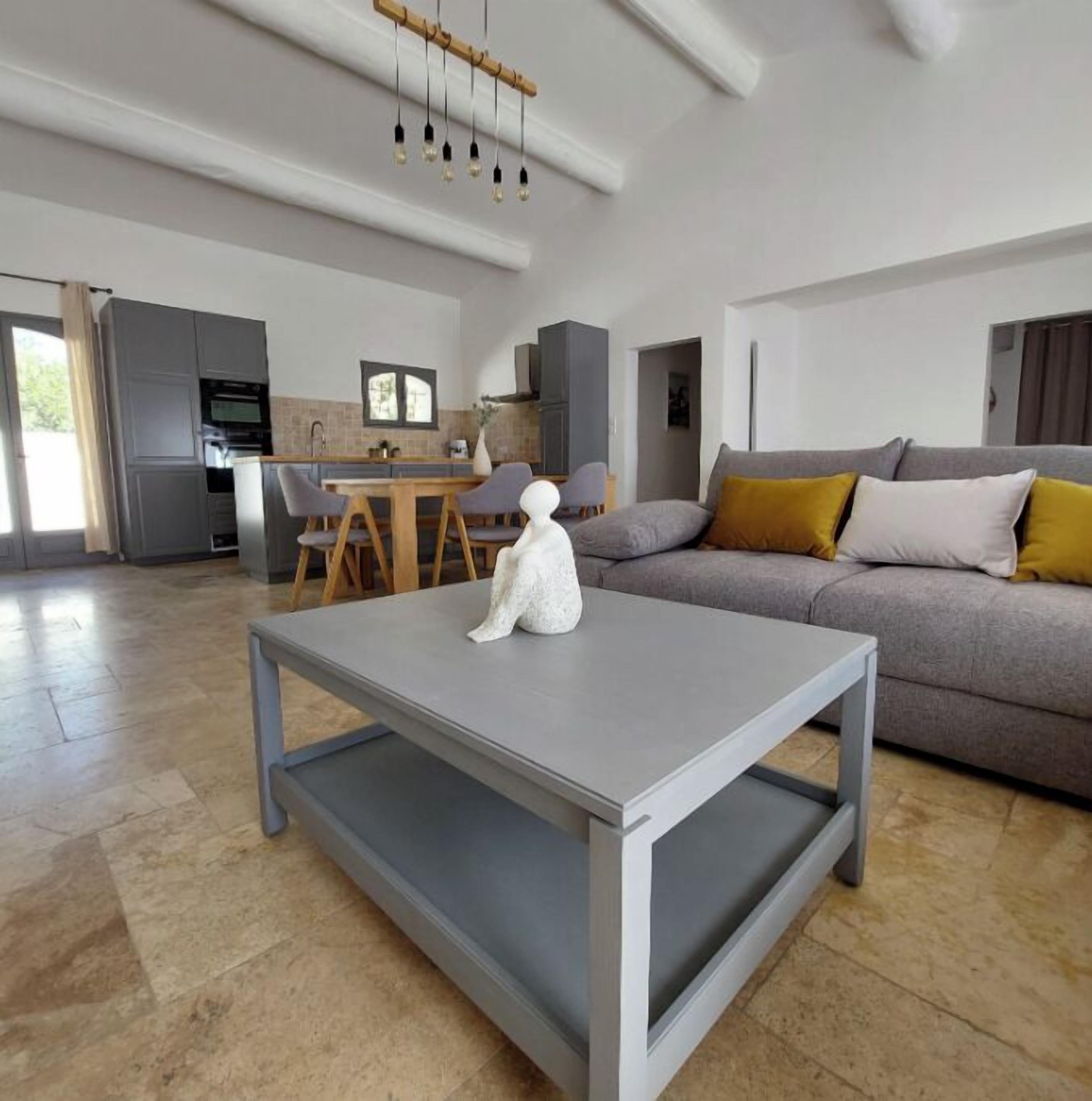 A modern living room with a grey sofa, a white coffee table, and a dining area with a wooden table and chairs.