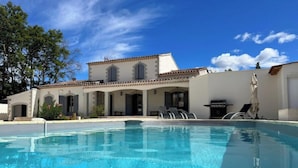 A swimming pool with lounge chairs and a patio area, surrounded by a building with a tiled roof and arches.