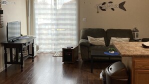 A living room with a wooden ceiling, a ceiling fan, a sofa, a coffee table, a TV on a stand, and a trash can.