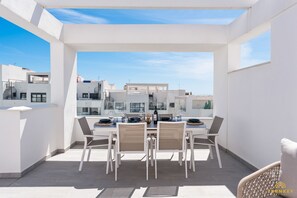 Une terrasse sur le toit, avec une table à manger pour quatre personnes, entourée de chaises blanches, d’où l’on peut admirer la vue sur la ville.