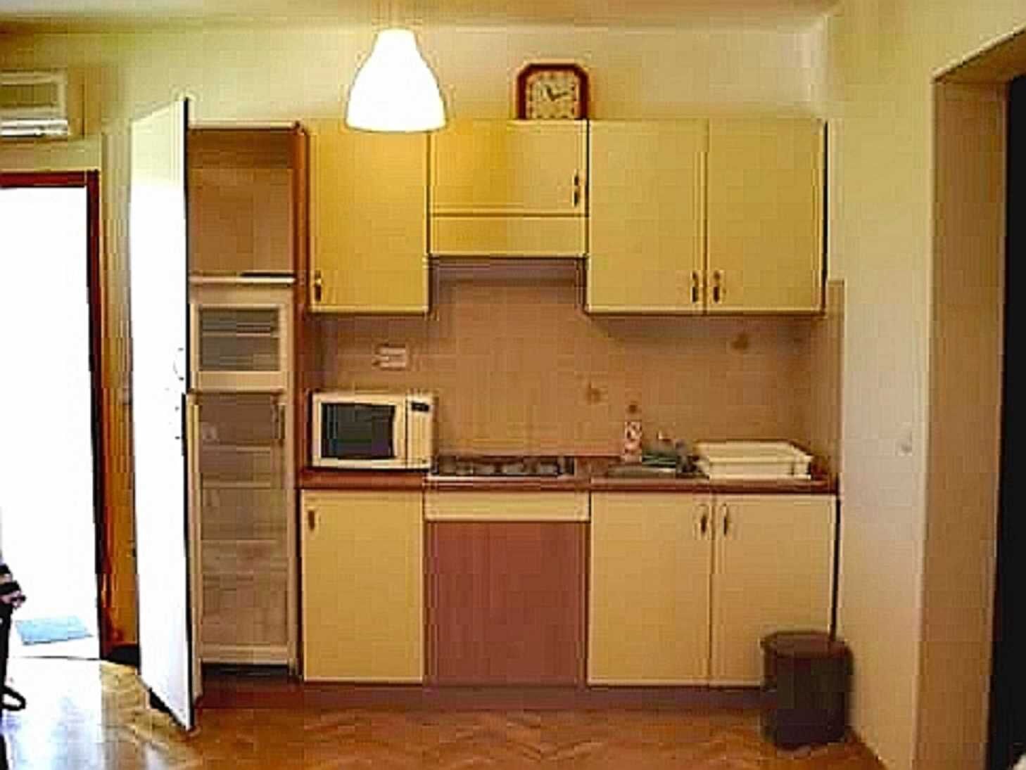 A compact kitchen with wooden cabinets, a microwave, and a clock on the wall.