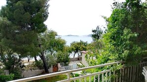 A balcony with a table set for two, overlooking a garden and a body of water. - Beach apartment Srima (Vodice)
