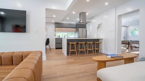 A modern living space with a sofa, a round wooden table, and a kitchen area with a bar stool set. - 5BR HotTub / PoolTable / MiniGolf / 7  min to Wynwood (Miami)