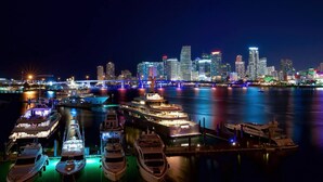 A marina with several yachts docked, a bridge, and a city skyline with illuminated buildings. - 5BR HotTub / PoolTable / MiniGolf / 7  min to Wynwood (Miami)